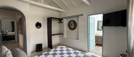 A bedroom with a checkered bedspread, a wooden wardrobe, a mirror, and a television on the wall.