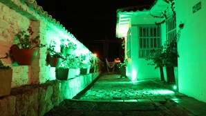 Een smalle steeg met een bakstenen muur aan één kant en een gebouw aan de andere kant, beide verlicht met groen licht.