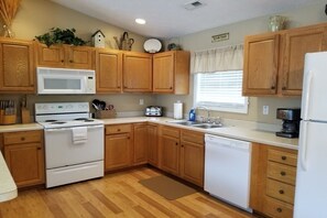 Una cocina con armarios de madera, microondas, estufa, lavavajillas y una ventana con persianas.