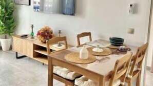 Uma área de refeições com uma mesa e cadeiras de madeira, uma TV de tela plana na parede e um vaso de planta.