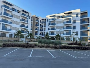 A multi-story residential building with balconies, a parking area, and a landscaped foreground. - Ideal apartment for families (Martil)