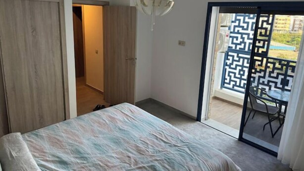 Quarto com cama, guarda-roupa, luminária no teto e vista para área externa com divisória de tela estampada.