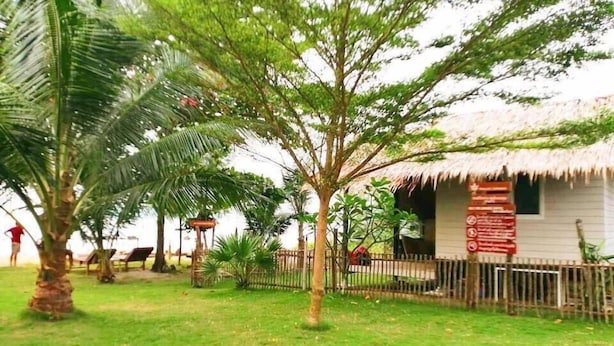 A grassy area with a palm tree, a thatched-roof structure, and a fenced area with a sign. - koh phaluai beach cottage (Chang Wat Surat Thani)