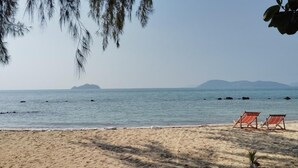 A beach with two sun loungers and a palm tree. - koh phaluai beach cottage (Chang Wat Surat Thani)