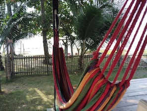 A hammock suspended between trees in a grassy area with a wooden fence in the background.