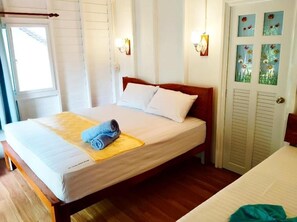 Una cama individual con estructura de madera, ropa de cama blanca y una toalla enrollada sobre un tapete amarillo.