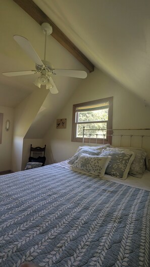 A bedroom with a sloped ceiling, a ceiling fan, a bed with a patterned bedspread, a window with blinds, and a chair. - Charming 2 BR Country Cottage - Peaceful Weekend Retreat Outside of Galena (Elizabeth)