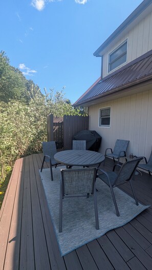 Een terras buiten met een tafel, stoelen, een barbecue en een houten schutting.
