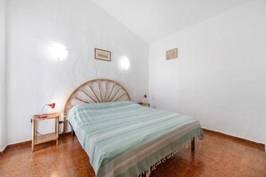 A room with a bed, a nightstand, two wall-mounted lamps, and a framed picture on the wall. - Casa Sosi - Costa Rei: Charming Holiday Home Near Beach with Garden and Sea View (Costa Rei)
