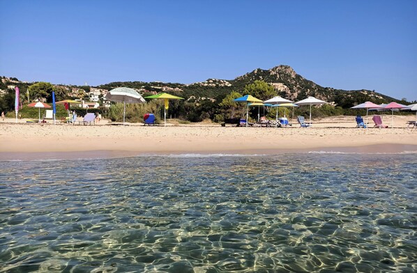 Une plage avec une eau claire, des parasols et des chaises longues.