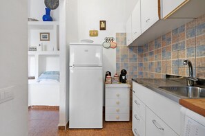 A compact kitchen with a white refrigerator, a sink, and a tiled backsplash. - Casa Sosi - Costa Rei: Charming Holiday Home Near Beach with Garden and Sea View (Costa Rei)