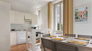 Moderni keittiö, jossa on valkoiset kaapit, ruokailutila neljän hengen ruokapöydällä sekä seinällä oleva taulu.