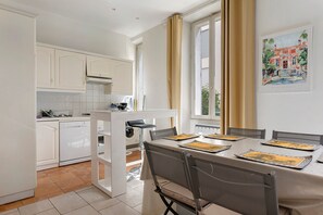 A modern kitchen with white cabinetry, a dining area with a table set for four, and a painting on the wall. - Apartment '2 Bedroom  Cannes Center' (Cannes)