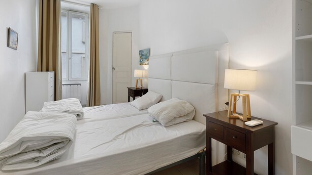 Hotellihuone, jossa on sänky, yöpöydät, lamppu, patteri ja ovi.
