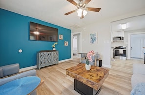 A modern living room with a blue accent wall, a wooden coffee table with a vase, a grey sofa, and a ceiling fan.