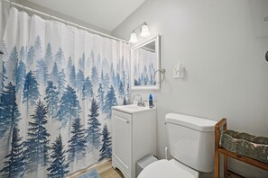 Une salle de bain avec un rideau de douche orné d’un motif de forêt, un lavabo avec un miroir au-dessus et des toilettes.