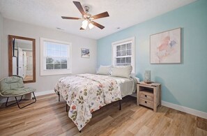 Ein Schlafzimmer mit Bett, Stuhl, Nachttisch, Deckenventilator und Fenster.