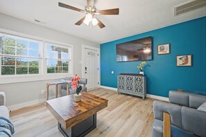 Ein modernes Wohnzimmer mit Couchtisch aus Holz, grauen Sofas, einer blauen Akzentwand und einem Deckenventilator.
