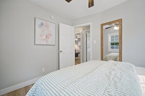 A bedroom with a bed, a door, a mirror, and a painting on the wall. - Cozy Buckroe Beach Bungalow - 2BR Near Sand, Dining & Family Fun. (Hampton)