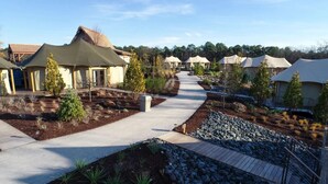 A pathway leading to multiple tents with a thatched roof, surrounded by landscaped gardens and a clear sky.