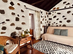 A room with a stone-patterned wall, a bed with a patterned rug, a wicker chair, and a wooden nightstand.