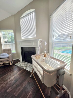 A room with a fireplace, a crib, and a rocking chair. - Grand Conroe Retreat Near The Woodlands, Pool, 2 Primary Suites, Sleeps 8 (Conroe)