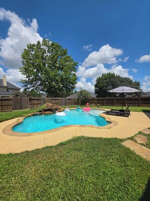 A backyard with a swimming pool, a wooden fence, and a large tree. - Grand Conroe Retreat Near The Woodlands, Pool, 2 Primary Suites, Sleeps 8 (Conroe)