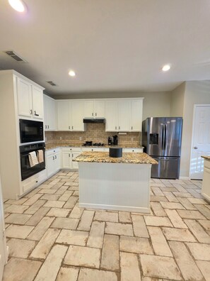 A kitchen with white cabinets, a granite countertop, a stainless steel refrigerator, and a herringbone-patterned floor. - Grand Conroe Retreat Near The Woodlands, Pool, 2 Primary Suites, Sleeps 8 (Conroe)