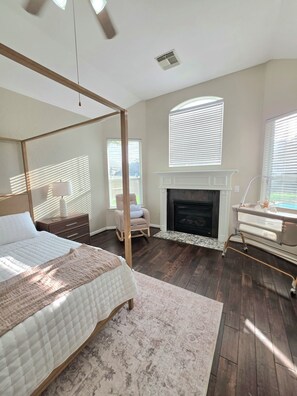 Une chambre à coucher avec un lit à baldaquin, une cheminée et une grande fenêtre équipée de stores.