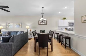 A modern living room with a sofa, dining table, and chairs, a kitchen area with cabinets and appliances, and a ceiling fan. - 2-bedroom apartment in charming Myrtle Beach with AC (Myrtle Beach)
