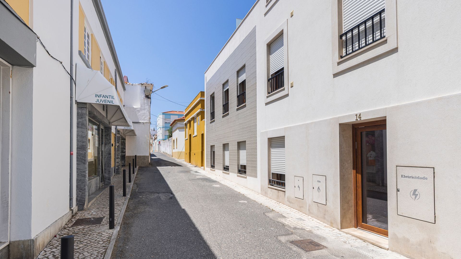A narrow street with buildings on either side, including a shop with a sign that reads 'INFANTIL JUVENIL'.