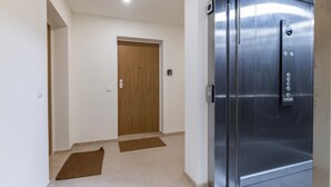 Een gang met een houten deur, een metalen lift en een deurmat op de vloer.