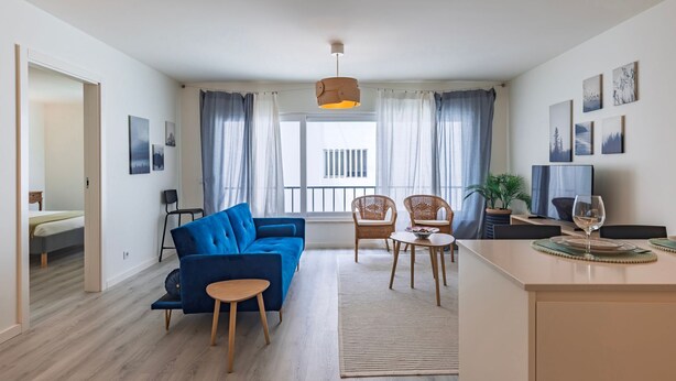 Een moderne woonkamer met een blauwe bank, twee rieten fauteuils, een kleine tafel en een televisie.