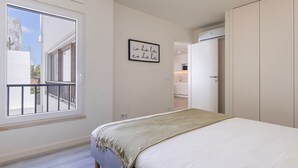 Een slaapkamer met een bed, balkon, keuken en een deur naar een andere kamer.