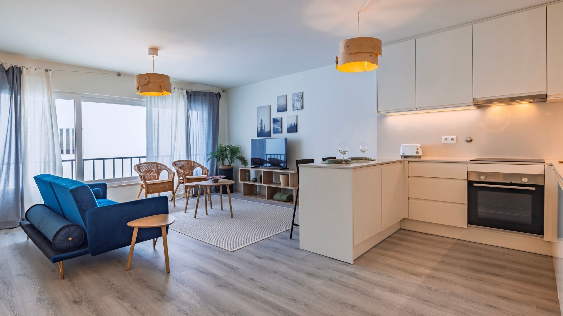 Un apartamento moderno con sala de estar, comedor y cocina. Hay sillas de mimbre, un sofá azul y un televisor de pantalla plana.
