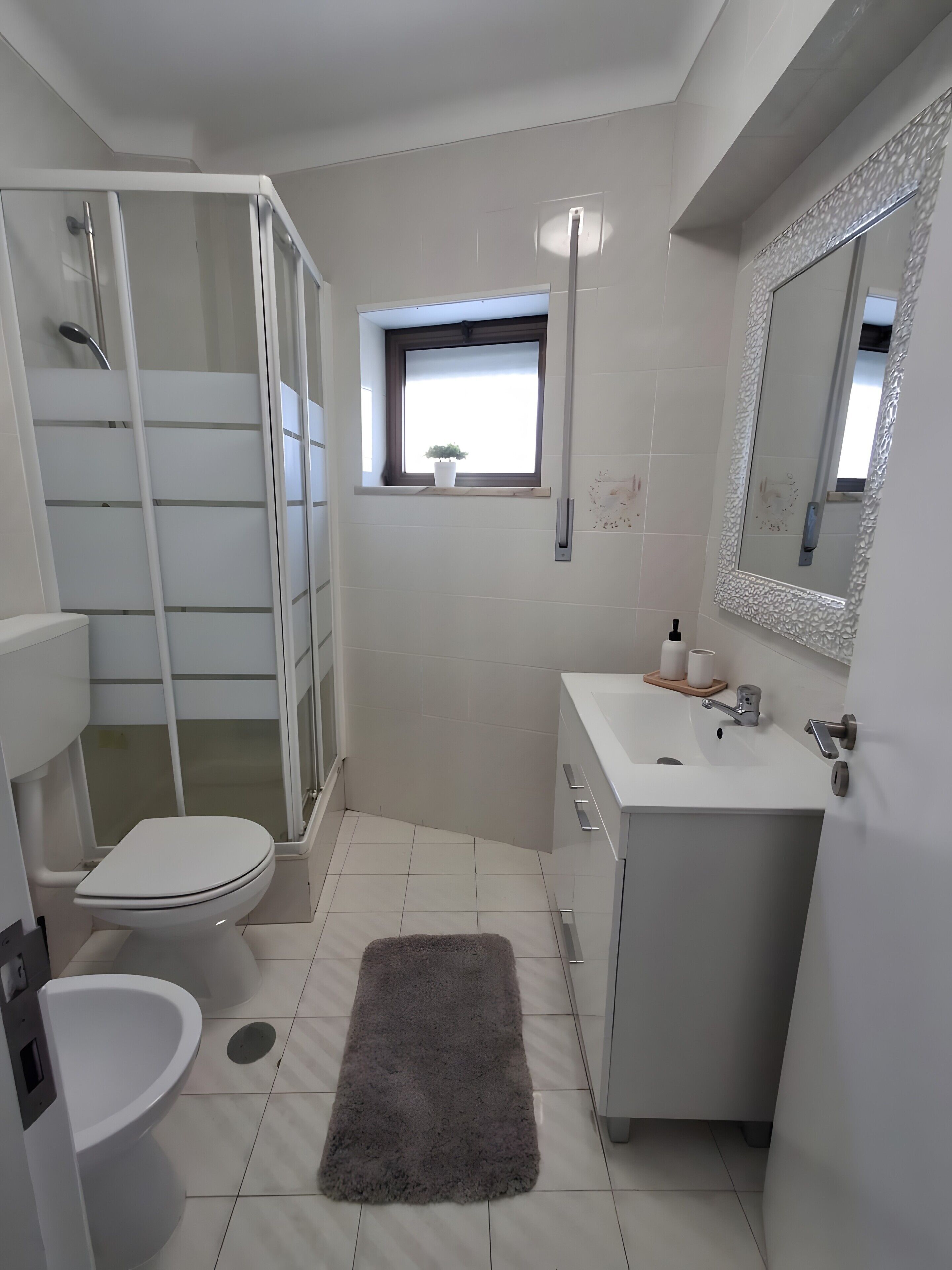 A modern bathroom with a shower enclosure, toilet, sink, and a small window with a plant.