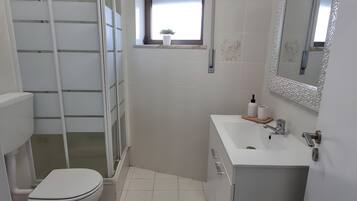 A modern bathroom with a shower enclosure, toilet, sink, and a small window with a plant.