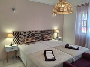 Habitación de hotel con cama, dos mesitas de noche, lámpara colgante y ventana con cortinas.