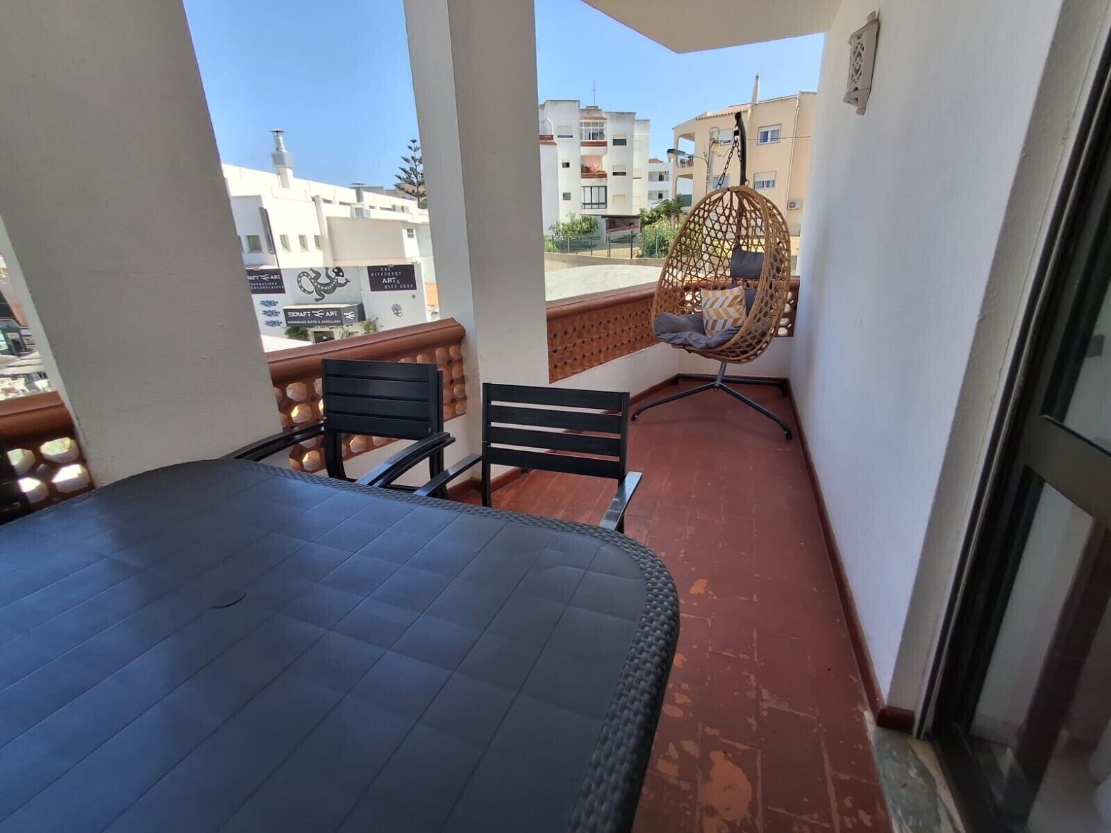 Un balcón con mesa y sillas, una silla colgante y vistas de edificios al fondo.