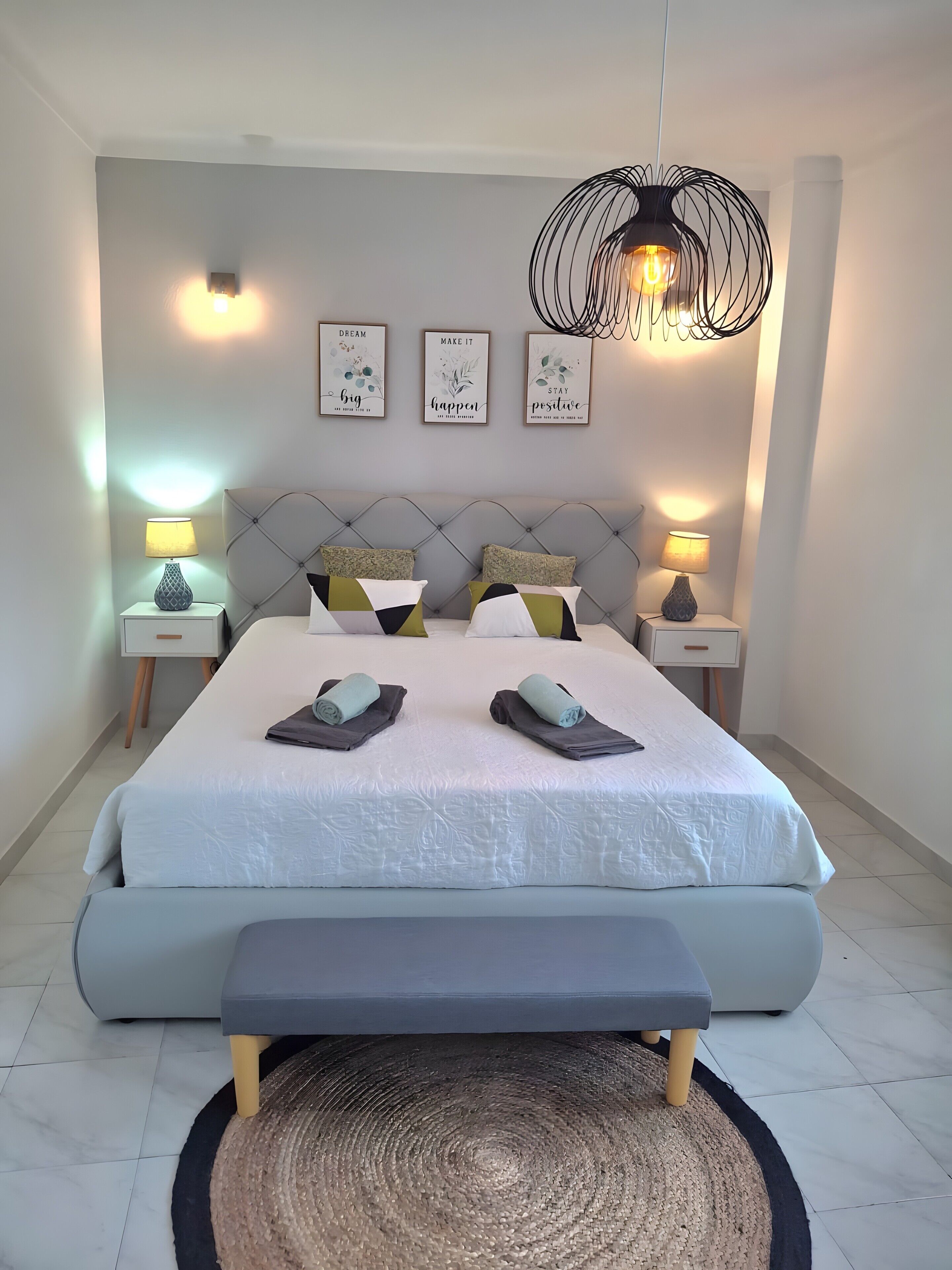 Een moderne slaapkamer met een groot bed, twee nachtkastjes, een bankje en een hanglamp.