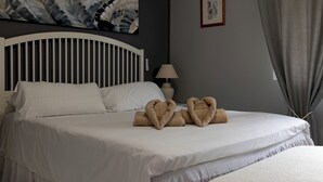 Hotellihuone, jossa on sänky, tyynyjä, yöpöytälamppu, taulu seinällä ja ikkuna, jossa on verhot.