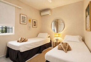 A hotel room with two single beds, a round mirror, a wall-mounted air conditioner, and framed artwork. - La Pomonita - Two Bedroom Apartment, Sleeps 4 (Nerja)