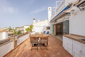 A rooftop terrace with a wooden table and chairs, a view of the city, and a white building with a blue and white facade. - La Pomonita - Two Bedroom Apartment, Sleeps 4 (Nerja)