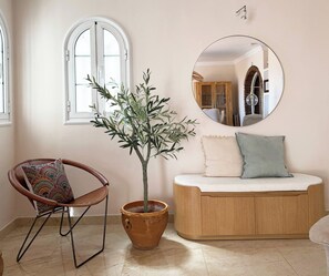 Une pièce comprenant un banc en bois, une plante en pot, une chaise avec un coussin à motifs et un miroir rond accroché au mur.