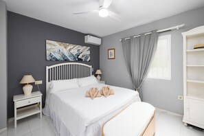 Une chambre à coucher moderne avec un lit, des tables de chevet, un ventilateur de plafond, un tableau et une armoire.