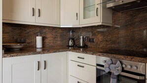 A kitchen with white cabinets, a granite countertop, a coffee maker, and an oven.