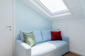 Ein hellblaues Sofa mit zwei Kissen, eines grün und eines rot, in einem Raum mit einem Oberlicht.