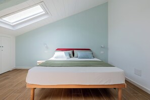 Ein Schlafzimmer mit schrägem Dach, einem Bett mit grüner Tagesdecke und Holzboden.