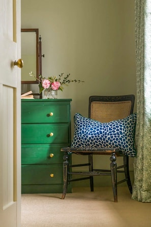 A room with a green dresser, a chair with a patterned pillow, and a mirror on the wall. - Lostwithiel Stable House (Boconnoc)
