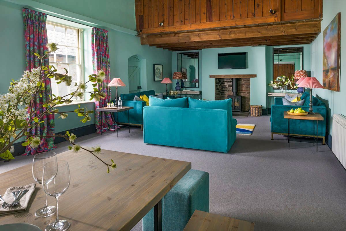 A cozy living room with a wooden ceiling, teal sofas, a dining table with chairs, and a fireplace.